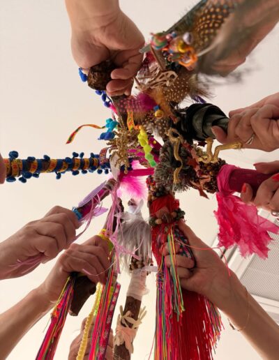 Mains tenant ensemble des branches ornées de fils, tissus et plumes.
