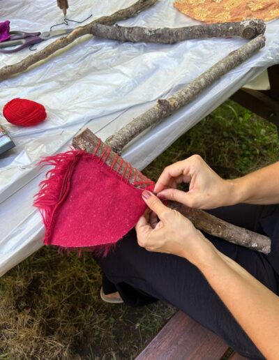 Mains cousant un morceau de tissu rouge à une branche.